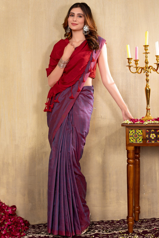 Woman in a red and purple saree standing next to a table with candles and flowers.
